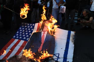 Demonstrator set fire to a sign depicting US President Donald Trump with the US and Israeli flags during a march in Medellin, Colombia